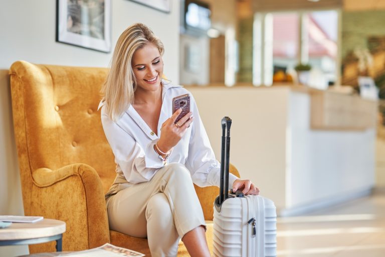 Putnica s kovčegom koristi mobitel u hotelskom lobbyju